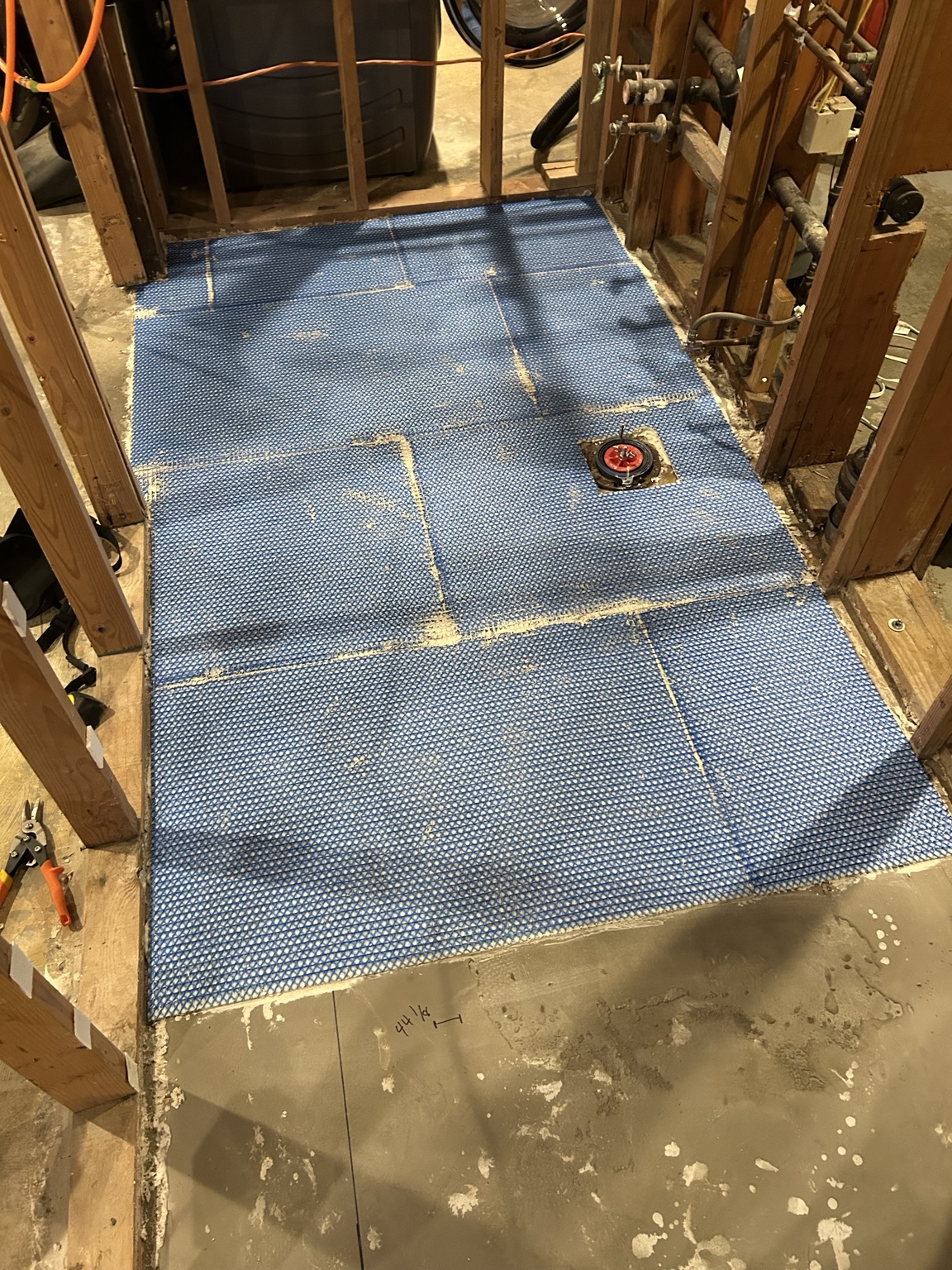 Blue uncoupling membrane installed around bathroom plumbing before floor tile